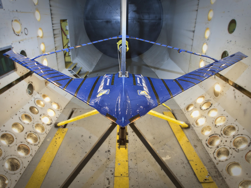 A blue glider is shownin a wind tunnel, tethered to its sides.