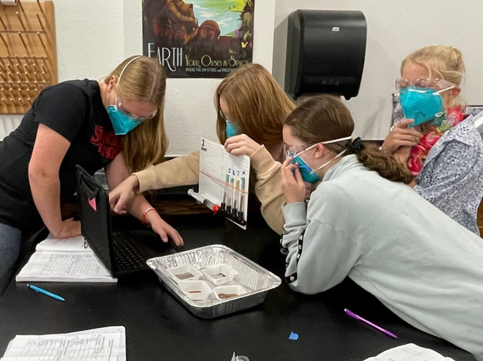 Image shows several students recording their experimental data, working together and possibly rewatching a recording. 