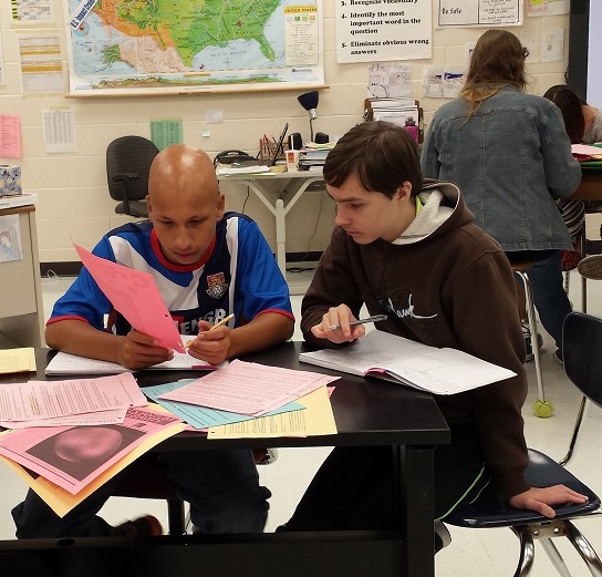 Two students in a classroom reading a colorful handout